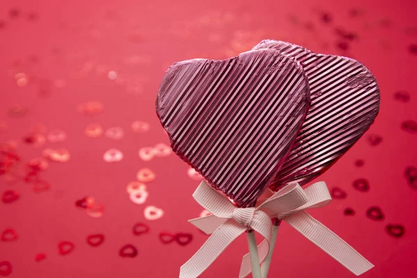 Valentin-napi koncepció, rózsaszín nyalóka alakú szív elszigetelt piros háttér, konfetti bokeh, másolás tér. — Stock Fotó