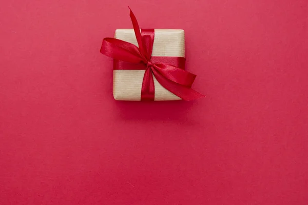 礼品盒用牛皮纸和红色弓包裹，红色背景隔离。 抽象平面铺装. — 图库照片
