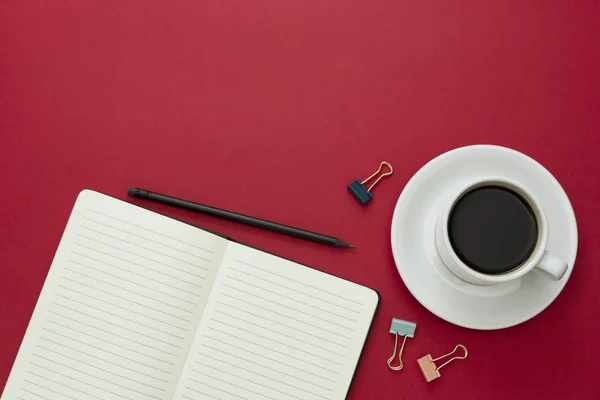 Επιφάνεια τραπεζιού, γραφείο εργασίας με ανοιχτό σημειωματάριο και φλιτζάνι καφέ σε κόκκινο φόντο. Αντιγραφή χώρου για κείμενο. — Φωτογραφία Αρχείου
