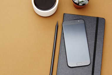 Masa üstü görünümü, ofis modeli, defter şablonu, kahve fincanı, sulu bitki ve kopyalama alanı olan akıllı telefon..
