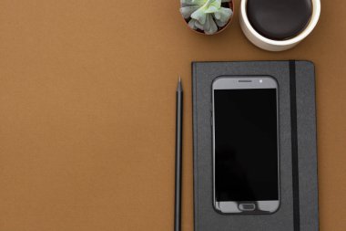 Masa üstü görünümü, ofis modeli, defter şablonu, kahve fincanı, sulu bitki ve kopyalama alanı olan akıllı telefon..