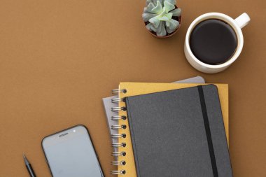 Masa üstü görünümü, ofis modeli, defter şablonu, kahve fincanı, sulu bitki ve kopyalama alanı olan akıllı telefon..