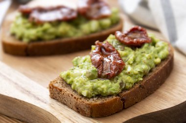 Vejetaryen yemeği. Guakomole ile çavdar ekmeği, avokado makarna ve kurutulmuş domates, tahta kesme tahtasında. Avokado tostu.