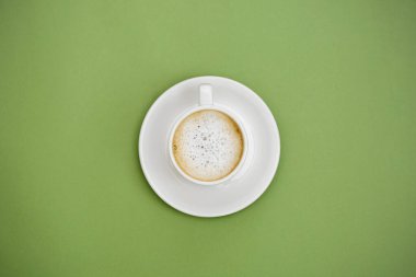 Beyaz bardakta sıcak sütlü kahve. Yeşil arka planda izole edilmiş. Boşluğu kopyala.