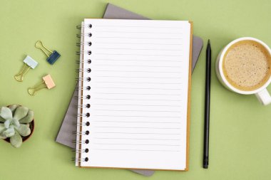 Boş sayfa ve kahve fincanı olan defteri aç. Masa üstü, yeşil arka planda çalışma alanı. Yaratıcı düz yatak.