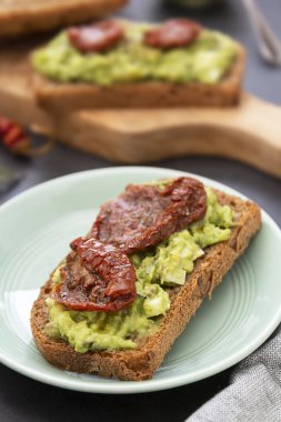 Sağlıklı yiyecekler. Guakomole ile çavdar ekmeği, avokado makarna ve kurutulmuş domates, tahta kesme tahtasında. Avokado tostu.