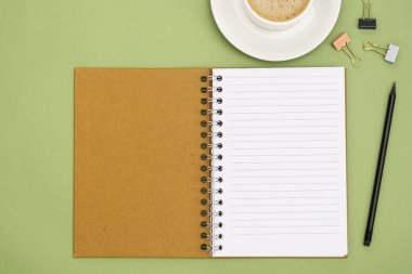 Boş sayfa ve kahve fincanı olan defteri aç. Masa üstü, yeşil arka planda çalışma alanı. Yaratıcı düz yatak.