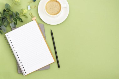 Boş sayfa ve kahve fincanı olan defteri aç. Masa üstü, yeşil arka planda çalışma alanı. Yaratıcı düz yatak.