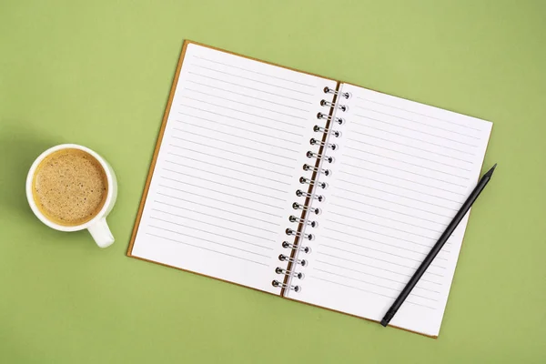 Offenes Notizbuch mit leerer Seite und Kaffeetasse. Tischplatte, Arbeitsbereich auf grünem Hintergrund. kreative flache Lage. — Stockfoto