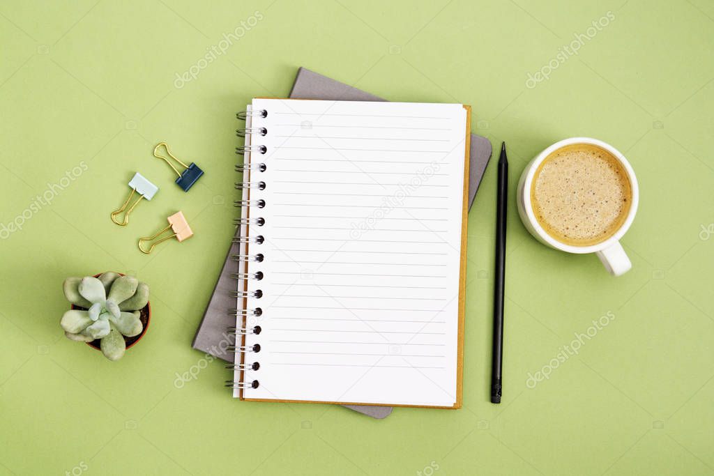 Open notebook with empty page and coffee cup. Table top, work space on green background. Creative flat lay.