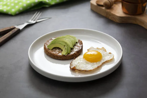 Avokádó pirított szendvics és egy tükörtojás egy fehér tányéron spárgával. Egészséges étel vagy reggeli. Sötét háttér. — Stock Fotó