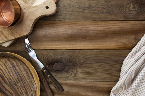 Bovenaanzicht van houten roodplaat met vork, mes, snijplanken op houten tafel. Geen afgedankte bestek. Kopieer ruimte, menu, recept of dieetconcept. — Stockfoto