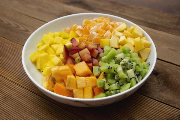 Fresh fruits salad - mango, citrus, kiwi fruit, plum and persimmon. Wooden background, flat lay, top view healthy food. Smoothie mix.