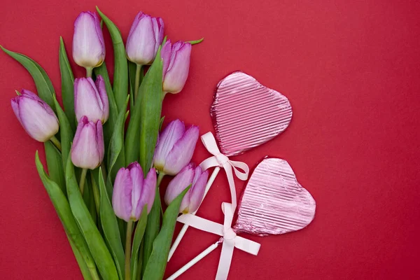 Flores de tulipán rosa o púrpura y chocolate en forma de corazón sobre fondo rojo. Vista superior con espacio de copia. Concepto de San Valentín o Día de la Madre . — Foto de Stock