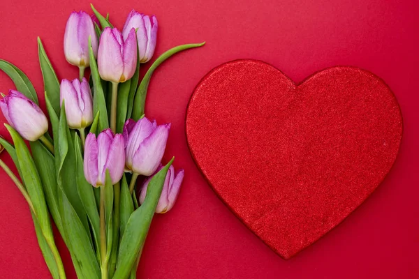 Rózsaszín vagy lila tulipán virágok és piros szív piros háttérrel. Felülnézet fénymásoló felülettel. Valentin-nap vagy anyák napja koncepció. — Stock Fotó