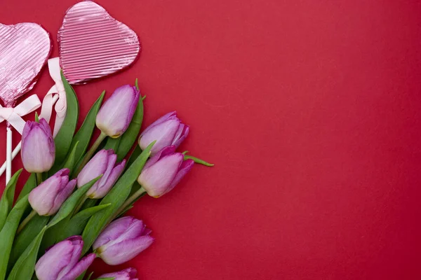 ピンクまたは紫のチューリップの花や赤い背景にハート型のチョコレート。コピースペース付きのトップビュー。バレンタインデーや母の日のコンセプト. — ストック写真