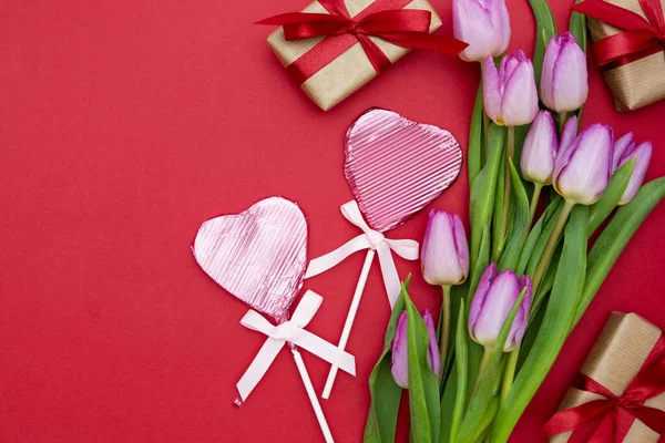 Rosa eller lila tulpanblommor, hjärtformad choklad och presentaskar på röd bakgrund. Ovanifrån med kopieringsutrymme. Alla hjärtans dag eller mammas dag koncept. — Stockfoto