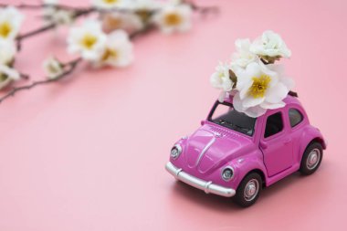 Corby, İngiltere 7 Şubat 2020. Pembe arka planda bahar, yaz çiçekleri olan minyatür pembe oyuncak araba. Minimum konsept. Boşluğu kopyala.