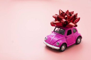 Corby, İngiltere 7 Şubat 2020. Pembe arka planda kırmızı kurdeleli minyatür pembe oyuncak araba..