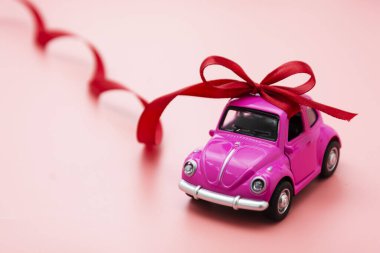 Corby, İngiltere 7 Şubat 2020. Pembe arka planda kırmızı kurdeleli minyatür pembe oyuncak araba..