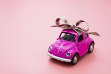 Corby, İngiltere 7 Şubat 2020. Pembe arka planda rustik kurdele yaylı minyatür pembe oyuncak araba..
