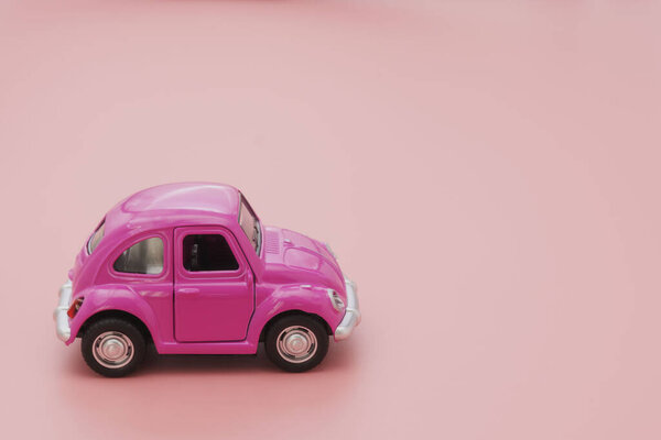 Corby, UK February 7, 2020. Миниатюрный розовый игрушечный автомобиль на розовом фоне. Транспортная концепция. Копирование пространства
.