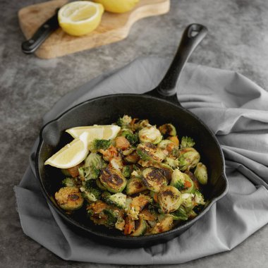 Demir tavada kızartılmış Brüksel lahanası ve limon dilimleri. Karanlık arka plan. Kare görüntü. Sağlıklı gıda konsepti.