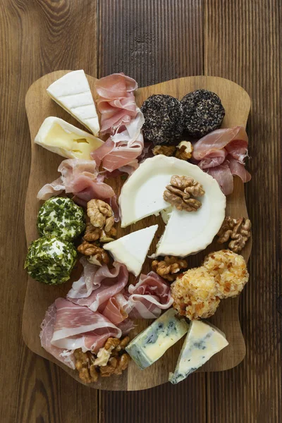 Prato de queijo, vários tipos de queijos, uvas, nozes e mel e presunto. Placa de corte de madeira . — Fotografia de Stock