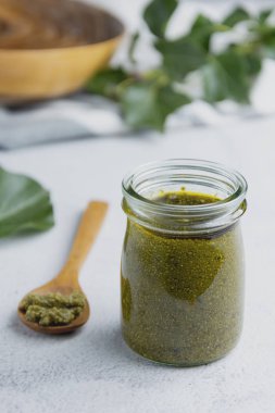 Beyaz desenli arka plan masasında pesto soslu cam kavanoz. Makarna sosu.