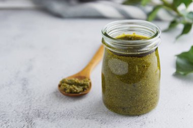 Beyaz desenli arka plan masasında pesto soslu cam kavanoz. Makarna sosu. Boşluğu kopyala.