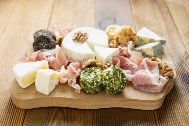 Çeşitli peynir, üzüm, ceviz, bal ve prosciutto çeşitleri. Tahta kesme tahtası.