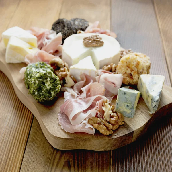 Vários tipos de queijos, uvas, nozes e mel e presunto. Placa de corte de madeira . — Fotografia de Stock