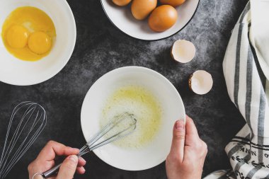 Omlet pişiriyorum. Bir kadının elleri taze bir yumurtayı kırıyor. Karanlık arka plan, besin düzlüğü