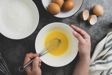 Bir kadının elleri yay içinde yumurta çırpar. Kahvaltıda omlet pişiriyorum. Yemek pişirme sürecinin en üst görüntüsü. Koyu arkaplan.