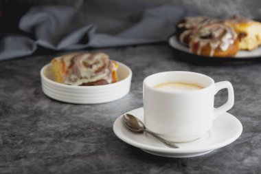 Bir fincan sade kahve ve tarçınlı çörek, arka planda tarçınlı. Karanlık tahta.