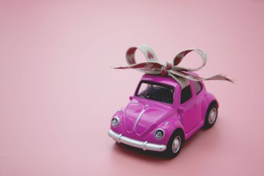 Corby, İngiltere 7 Şubat 2020. Pembe arka planda kurdeleli minyatür pembe oyuncak araba..