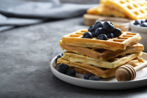 Stack of belgian waffles with blueberry and honey for breakfast. Delicious homemade pastry. Dark background.