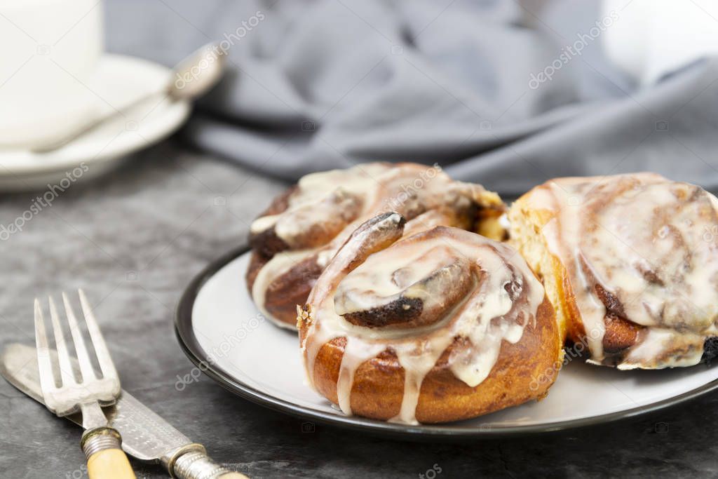 Cinnamon danish bun or cinnabons on dark background with coffee cup. Sweet, homemade pastry for breakfast.