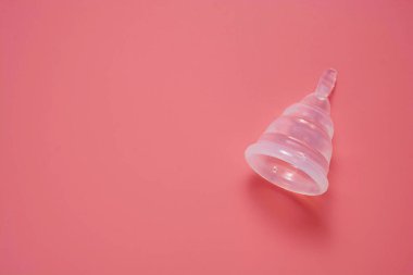 Pembe arka planda izole edilmiş regl bardağı. Kadın sağlık hizmetleri, yeniden kullanılabilir kadın hijyen ürünleri..