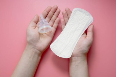 Adet öncesi hijyen ürünlerini tutan eller. Adet bardağı ve hijyenik ped. Sıfır atık alternatifi, seçim konsepti. Bakmak için.