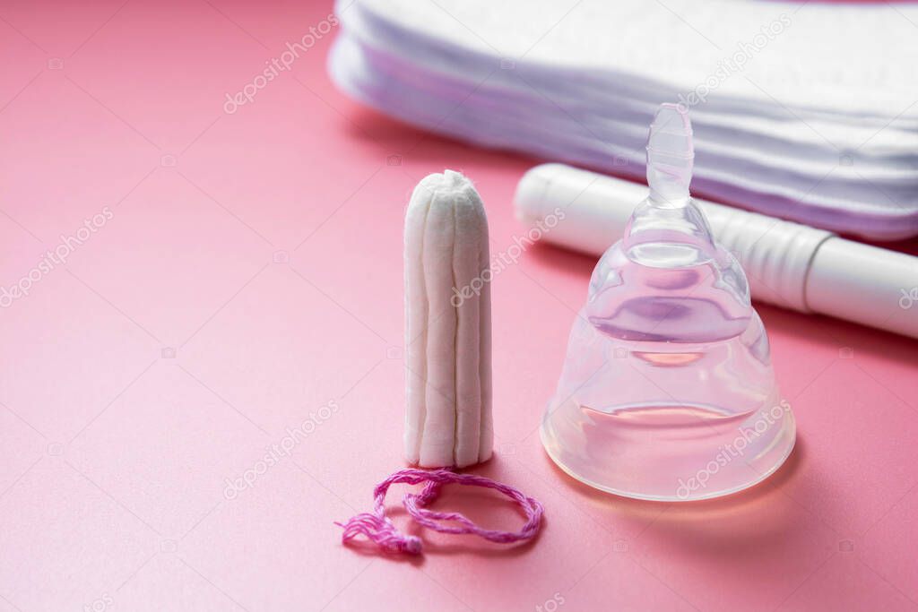Menstrual cup and feminine hygiene tampon, isolated on pink background. Feminine hygiene products with copy space.