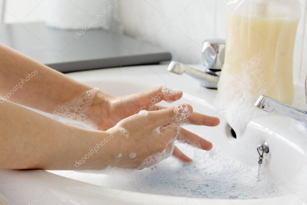 Close up of child's hand wash his hands over sink in bathroom.