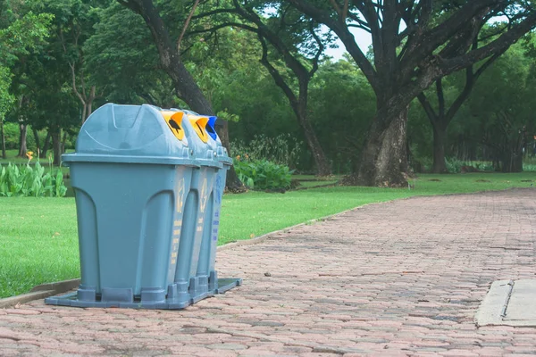 Public recycle bins or segregated waste bins located on concrete floor beside walkway in public park with green natural background. (Vintage style)