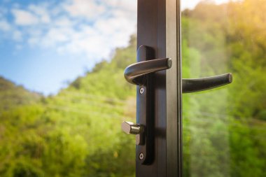 Kapı kolu açılan siyah modern cam kapı ile yeşil doğal ve blus gökyüzü arka plan kapatın. (Seçici odak)