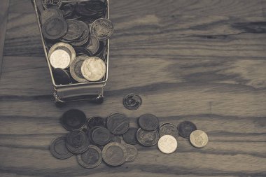 İş ve Finans kavramı: sarı mini alışveriş sepeti ya da süpermarket arabası para sikke yığını yanında vintage tarzı ahşap tablo olarak çeşitli para sikke (Baht). (Seçici odak)