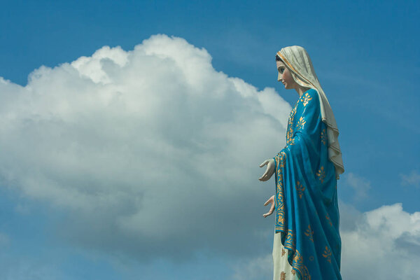 The Blessed Virgin Mary statue standing in front of The Cathedral of the Immaculate Conception at The Roman Catholic Diocese with crucifix and blue sky background at Chanthaburi Province, Thailand.