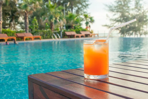 Summer Vacation Concept : Welcome drink orange juice punch put on wooden table nearly swimming pool with blue water and daybed in background.