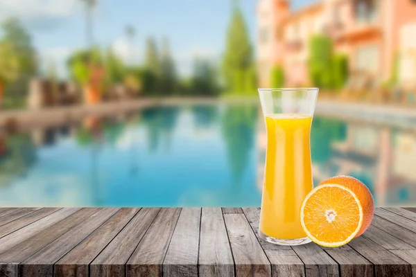 Summer Vacation Concept : Welcome drink orange juice punch put on wooden table nearly swimming pool with blue water and blue sky in background.