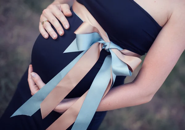 Mulher grávida segura mãos um estômago com arco — Fotografia de Stock