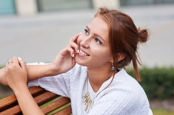 Schöne junge Frau sitzt auf einer Bank im Sommerpark — Stockfoto